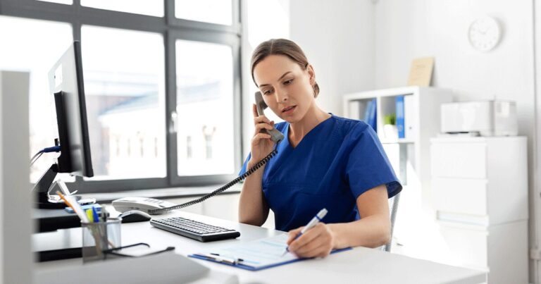 Healthcare professional talking on the phone while taking notes in a medical office, answering questions and providing guidance about early pregnancy symptoms and pregnancy testing.