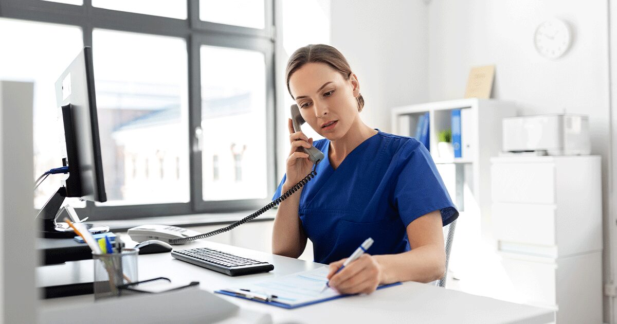 Healthcare professional talking on the phone while taking notes in a medical office, answering questions and providing guidance about early pregnancy symptoms and pregnancy testing.